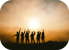 Seis personas con los brazos levantados durante un amanecer en un campo, con un cielo naranja y el sol en el horizonte.